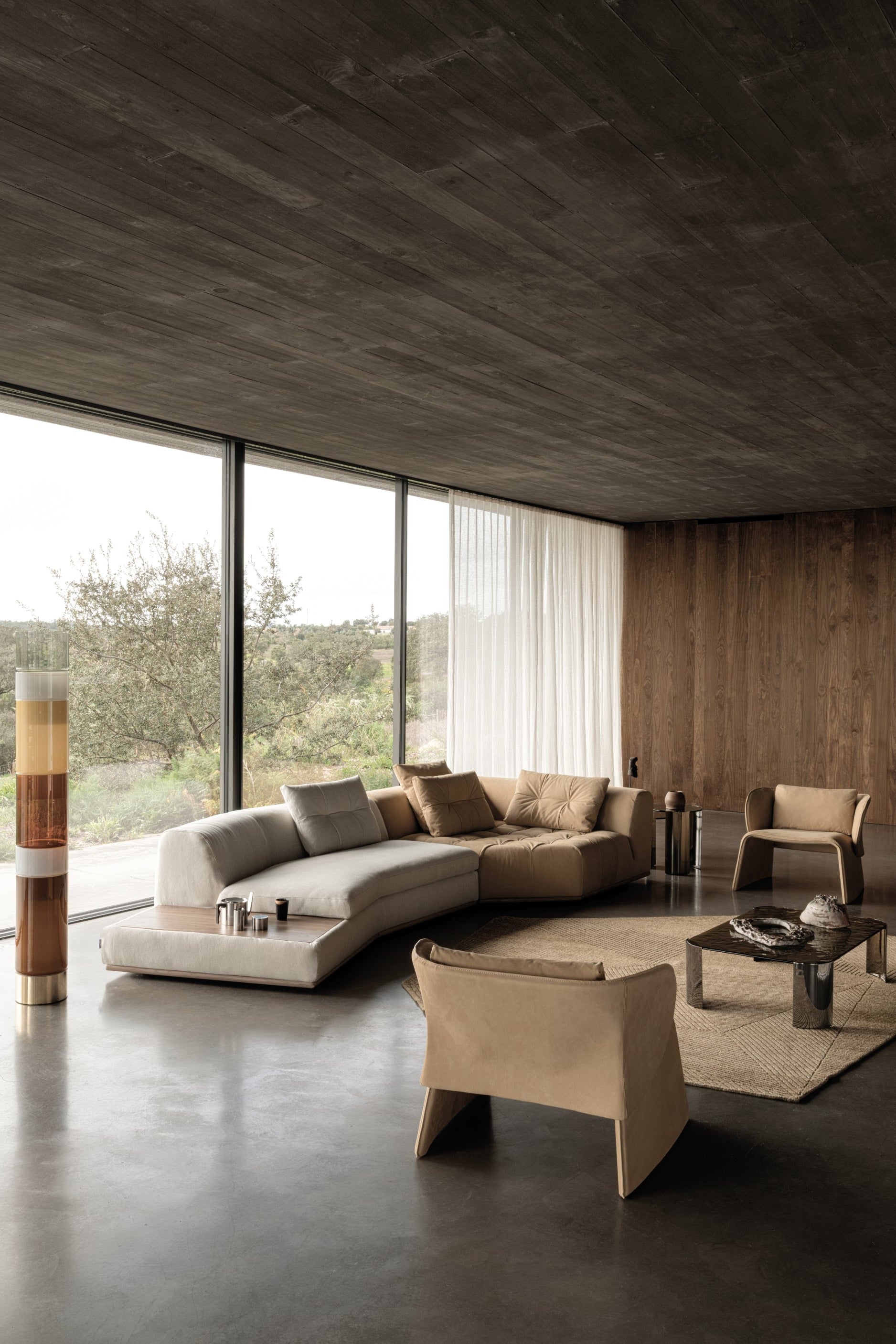 Modern living room with a curved sofa, armchair, and large windows.